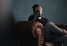 a man holds his head while sitting on a sofa