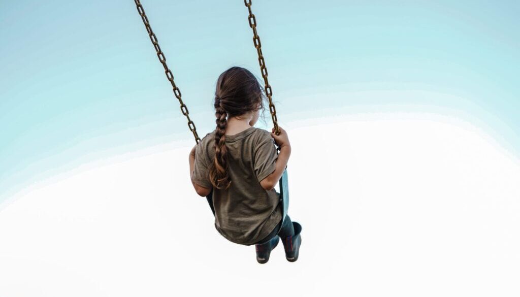 child in brown jacket sitting on swing during daytime