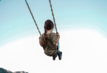 child in brown jacket sitting on swing during daytime