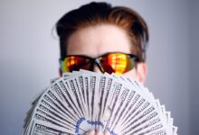 man in black framed sunglasses holding fan of white and gray striped cards
