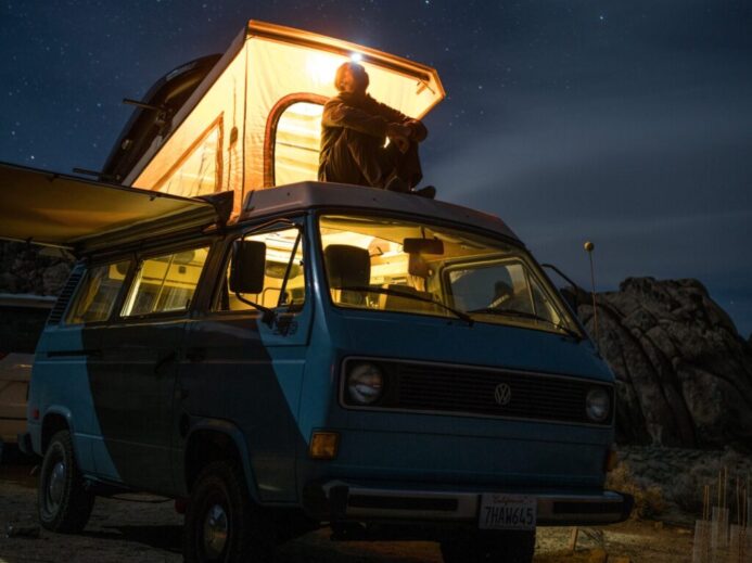 man sitting on top of blue van staring at sky during nighttime