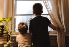 boy and girl standing near window looking outside