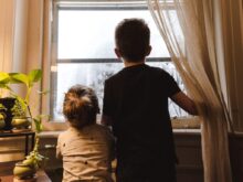 boy and girl standing near window looking outside