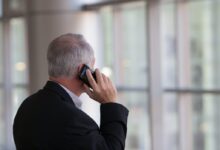 man holding black smartphone in front of a windowpane