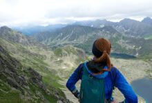 woman in blue jacket and black backpack standing on mountain during daytime