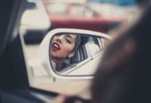 woman putting liquid lipstick on her lips while looking at vehicle's mirror during daytime