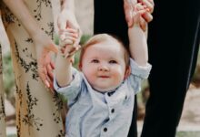 man and woman holding hand of toddler walking on grass field