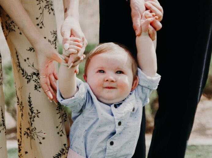 man and woman holding hand of toddler walking on grass field