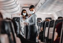 air hostess wearing a facemask standing in the aisle of an aeroplane