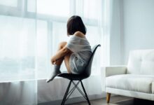 woman sitting on black chair in front of glass-panel window with white curtains