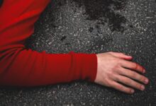 woman in red long sleeve shirt lying on black sand