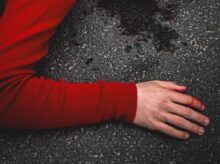 woman in red long sleeve shirt lying on black sand