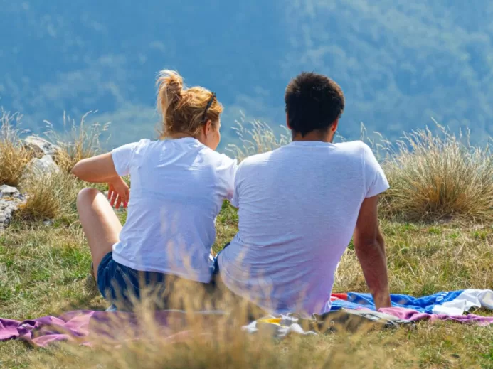 man iand woman in white shorts sitting on hill