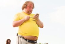 man in yellow shirt and brown pants using smartphone