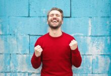 man wearing red long-sleeved shirt standing beside wall
