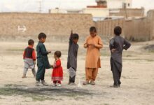 children in red and gray shirts standing on gray sand during daytime