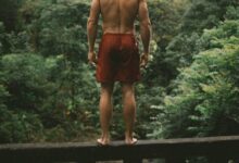 selective focus photography man in red shorts standing on bridge edge