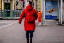 woman in red jacket walking on sidewalk during daytime