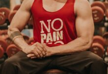 man in red tank top and black pants sitting on bench