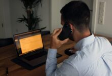 man in blue dress shirt holding black smartphone