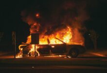 burning grey sedan near trees and signboard at night