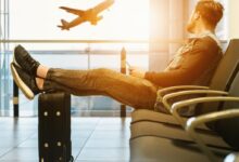 man sitting on gang chair with feet on luggage looking at airplane