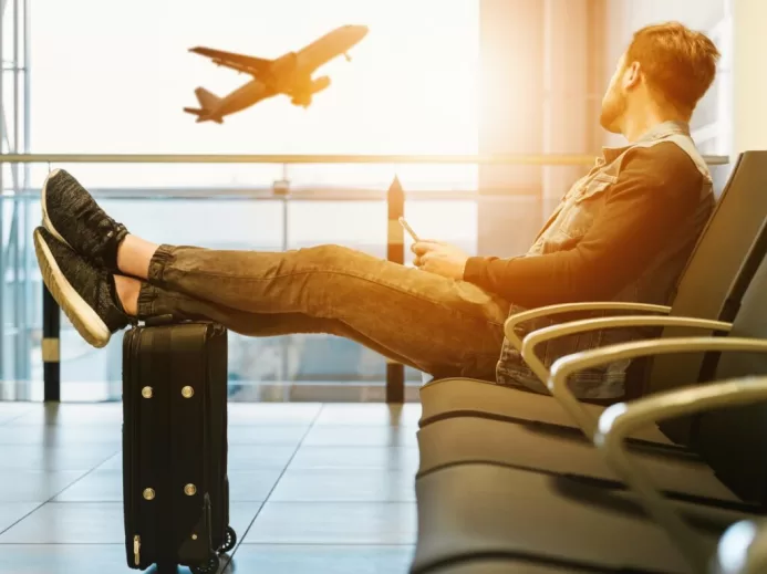 man sitting on gang chair with feet on luggage looking at airplane