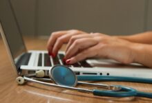 person sitting while using laptop computer and green stethoscope near