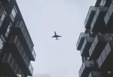 low-angle photography of airplane in flight over buildings
