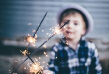closeup photo of boy wearing blue and white plaid sport shirt holding firework