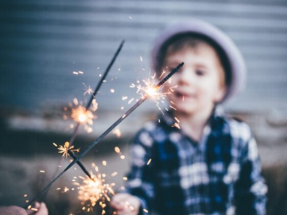 closeup photo of boy wearing blue and white plaid sport shirt holding firework