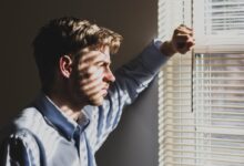 person near clear glass window pane and window blinds low-light photography