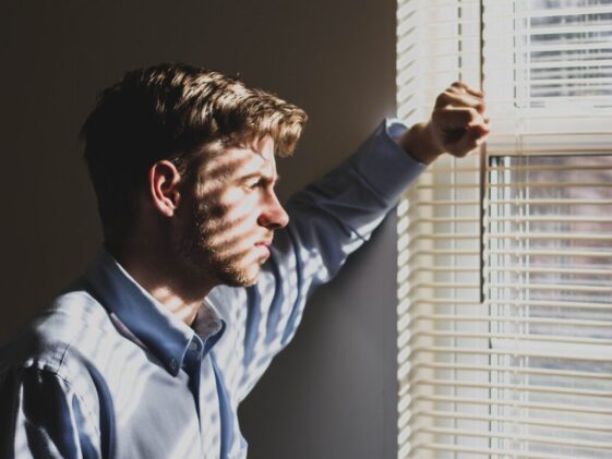 person near clear glass window pane and window blinds low-light photography