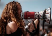 selective focus photography of woman wearing black cold-shoulder shirt using megaphone during daytime