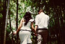 man and woman holding hands while walking near trees