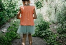 woman in pink tank top and blue denim shorts standing on pathway between green plants during
