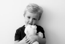grayscale photography of boy holding bear plush toy