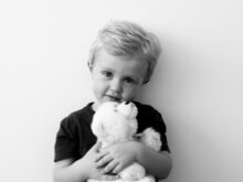 grayscale photography of boy holding bear plush toy