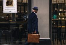 man in black suit jacket and blue hat standing in front of store