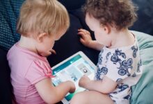 two toddlers sitting on sofa while using tablet computer