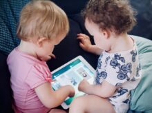 two toddlers sitting on sofa while using tablet computer