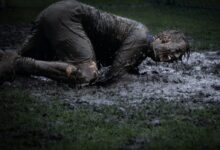 man lying on green grass soaked with mud