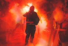 man in black jacket standing on stage with red lights