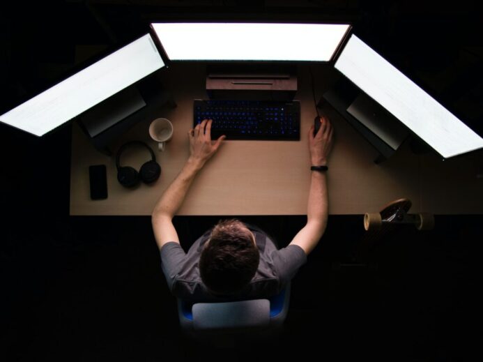 man facing three computer monitors while sitting
