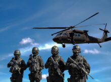 Four Soldiers Carrying Rifles Near Helicopter Under Blue Sky