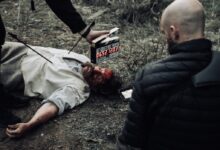 man in black bubble jacket facing man in white shirt lying on the ground while man in black bottoms holding digital time device
