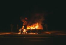 burning grey sedan near trees and signboard at night