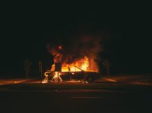 burning grey sedan near trees and signboard at night