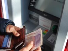 person holding brown leather wallet and banknotes