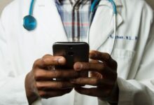 person wearing lavatory gown with green stethoscope on neck using phone while standing